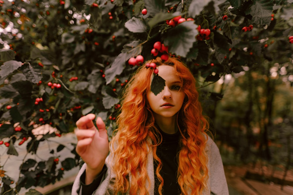 a woman with long red hair standing in front of a tree