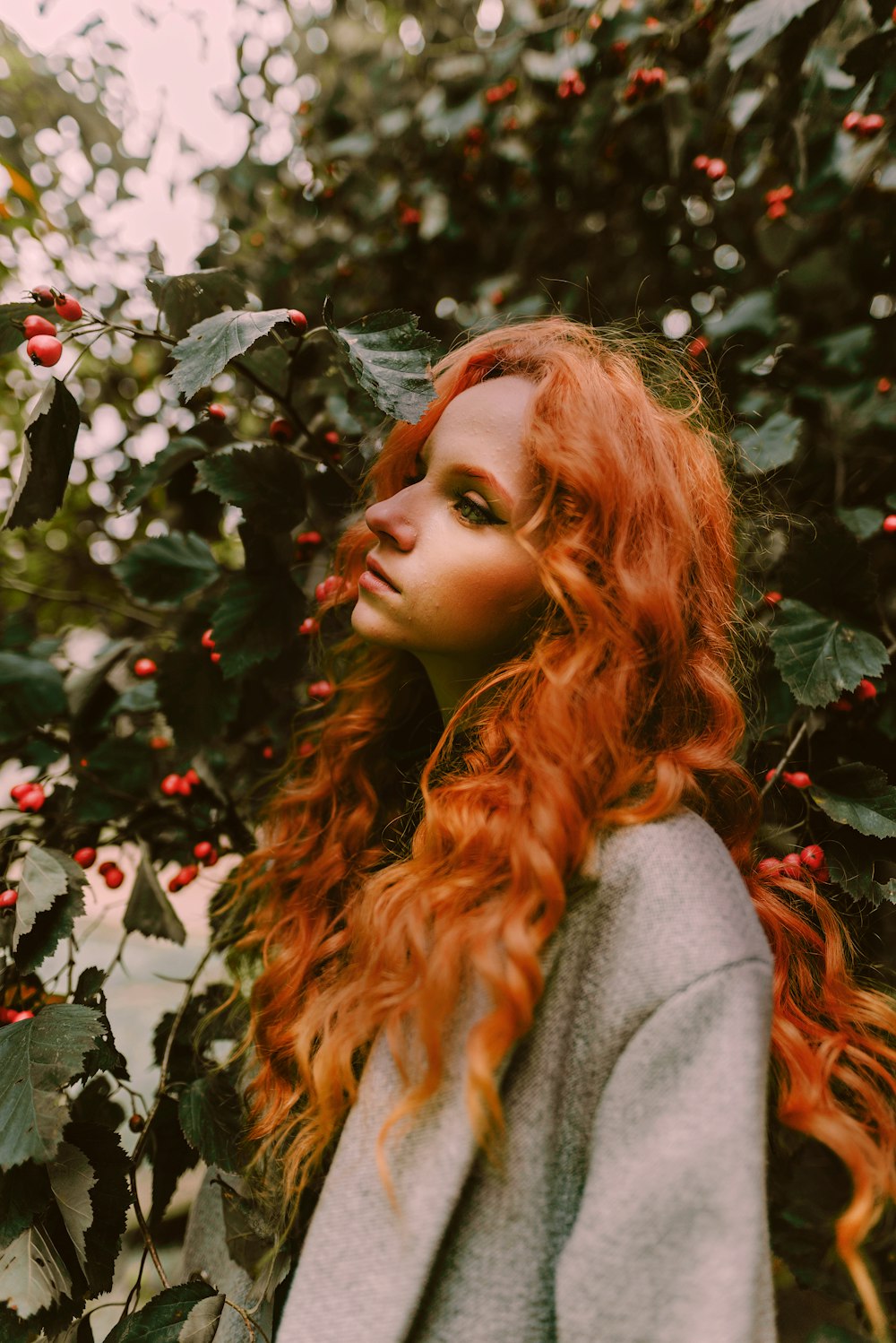 a woman with long red hair standing in front of a bush