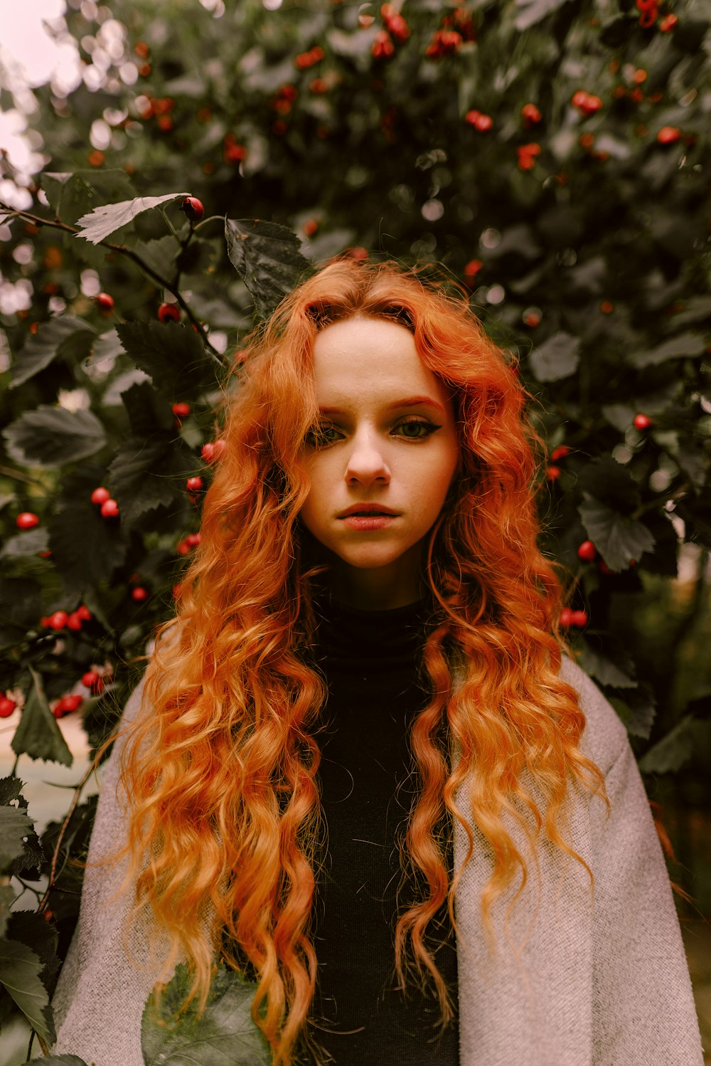 a woman with red hair standing in front of a bush