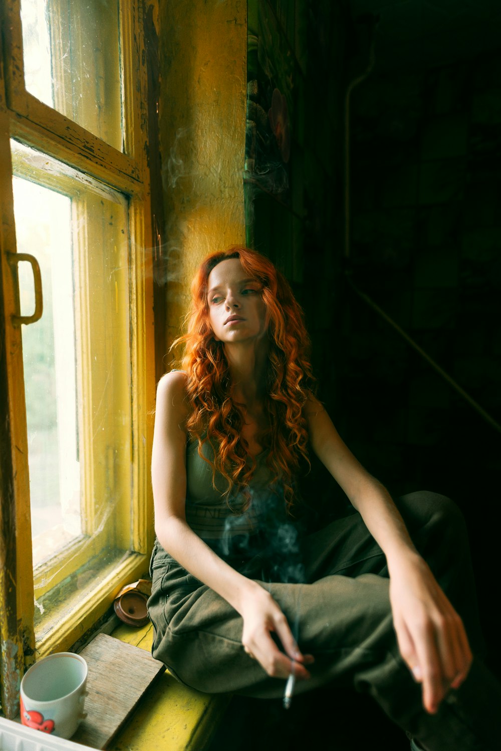 a woman sitting on a window sill smoking a cigarette