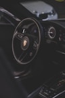A luxury car interior focusing on the steering wheel with a recognizable logo, alongside the dashboard with modern instruments. The environment is dimly lit, providing a sleek and sophisticated ambiance.