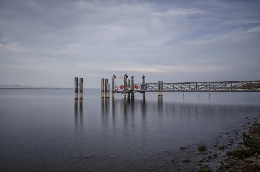 a long pier sitting on top of a lake under a cloudy sky