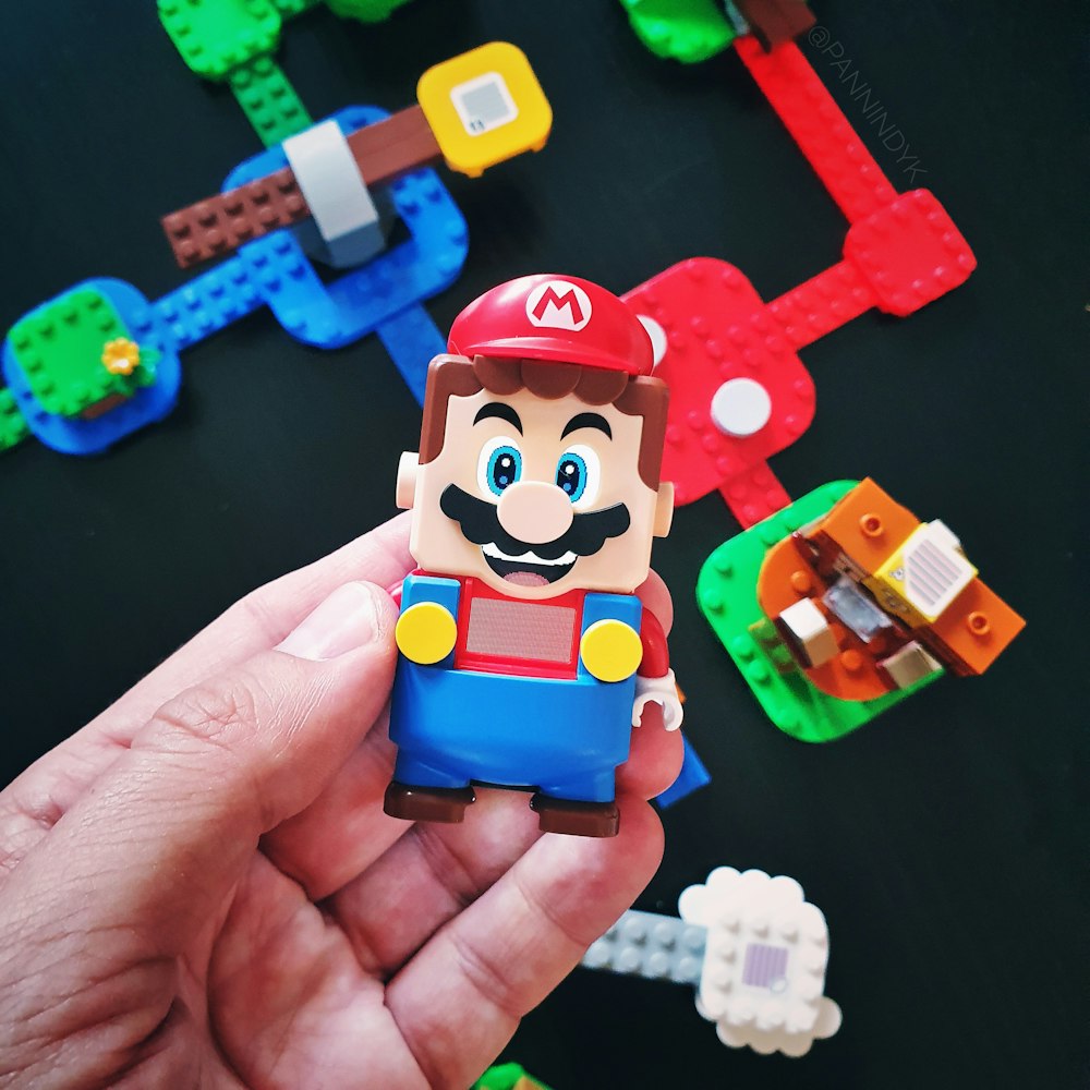 a hand is holding a toy of a mario