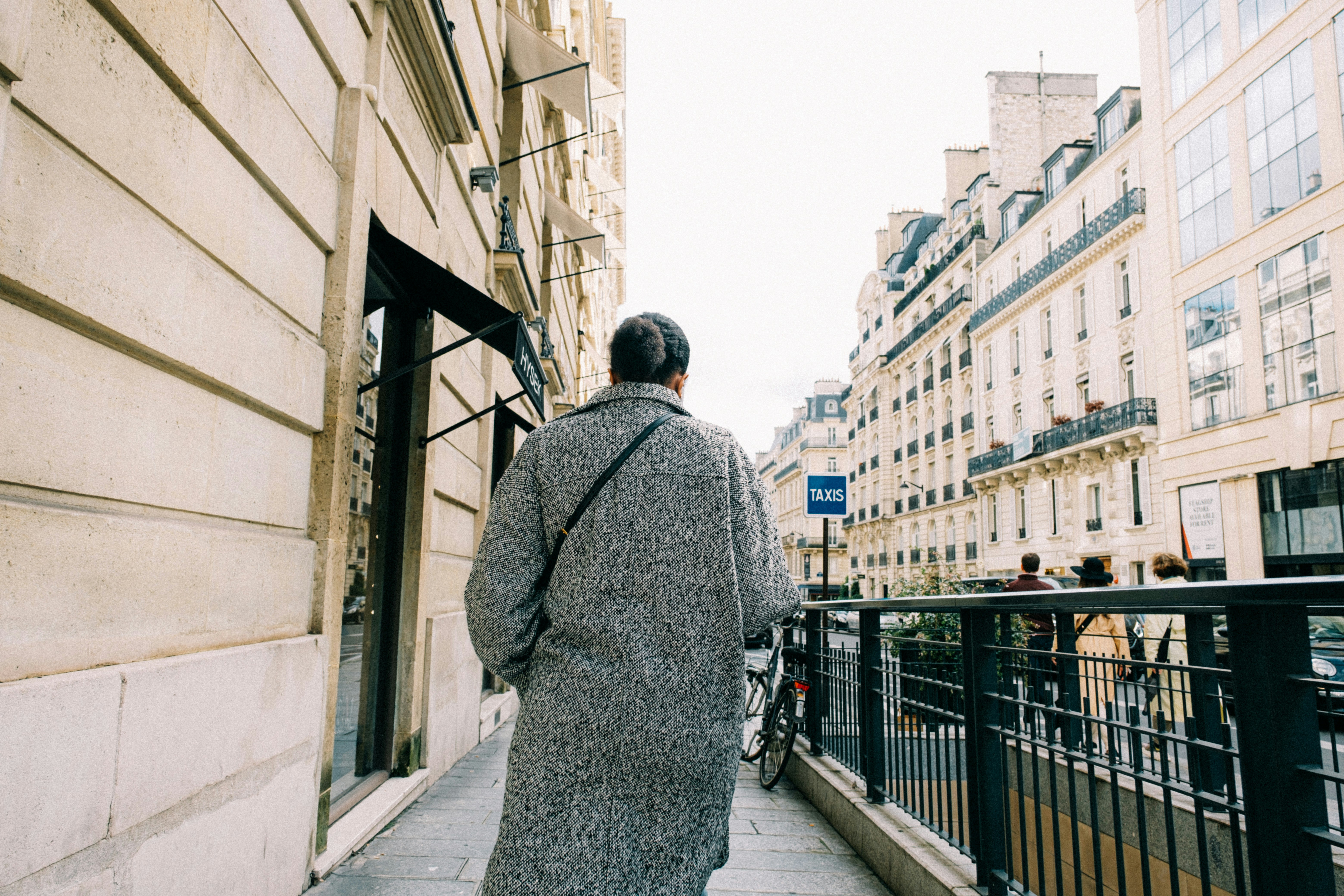 a woman walking down a sidewalk next to tall buildings