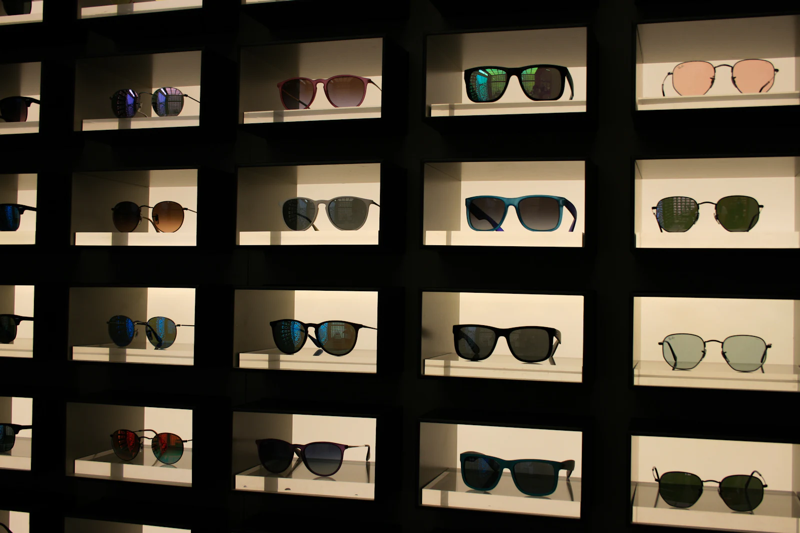 Sunglasses set out on lit shelves in a dark shop.