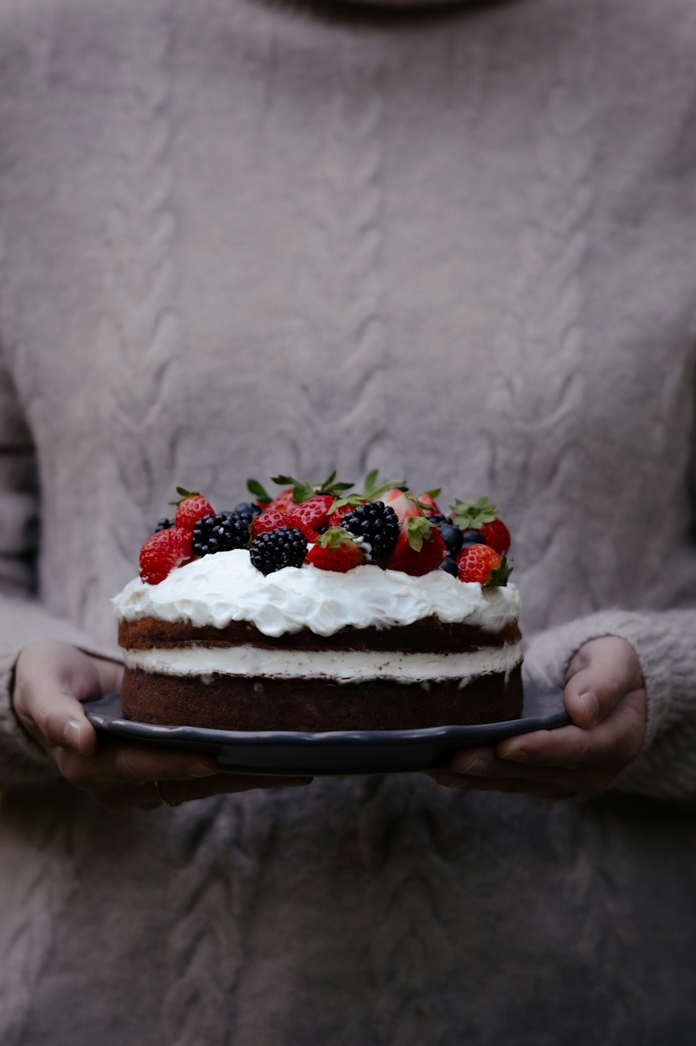 a person holding a cake with fruit on top
