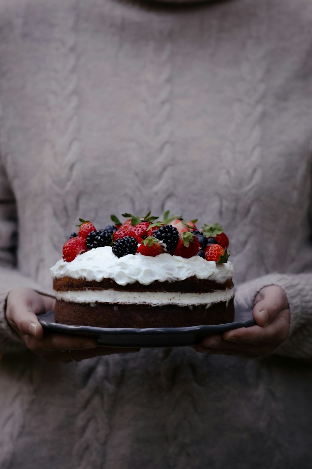 une personne tenant un gâteau avec des fruits sur le dessus