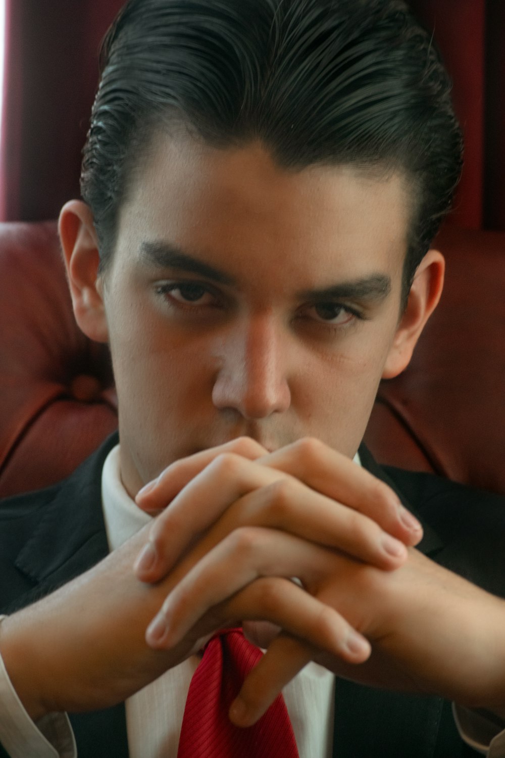 a man in a suit and red tie sitting in a chair