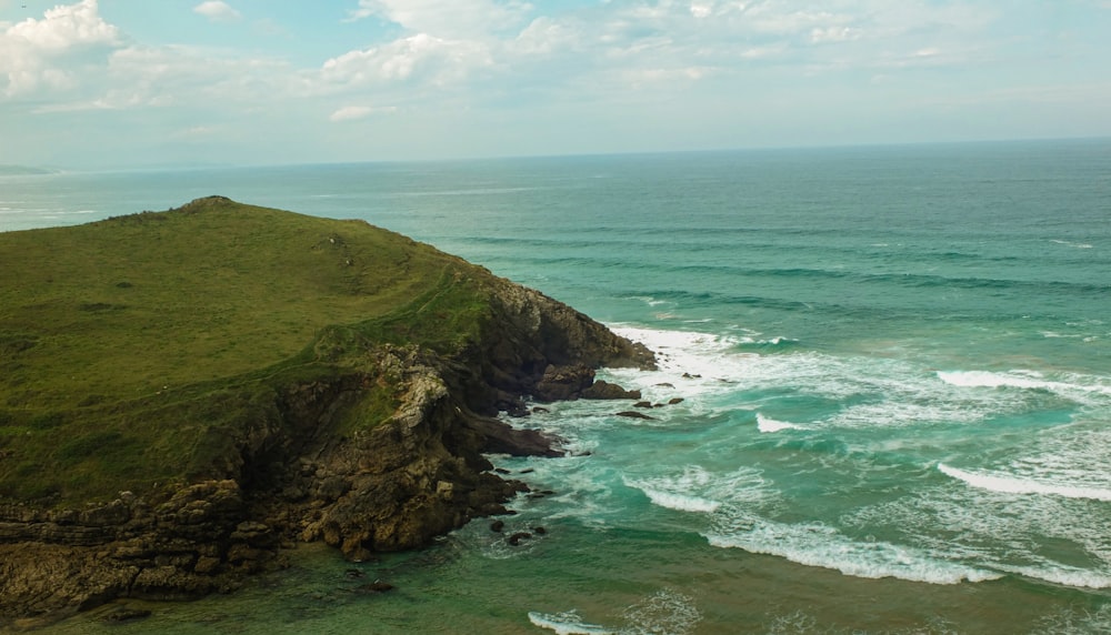 an aerial view of the ocean and a grassy hill