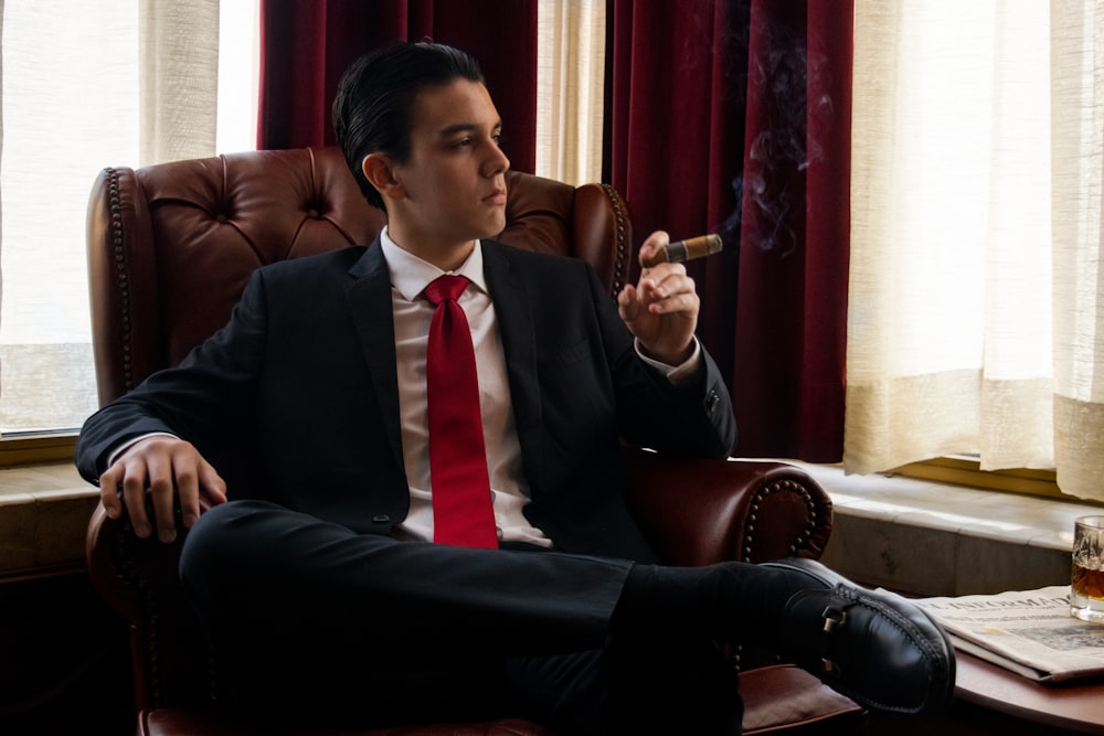 Un hombre sentado en una silla fumando un cigarrillo