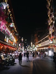 A lively cityscape at night with people meeting and chatting under warm streetlights.