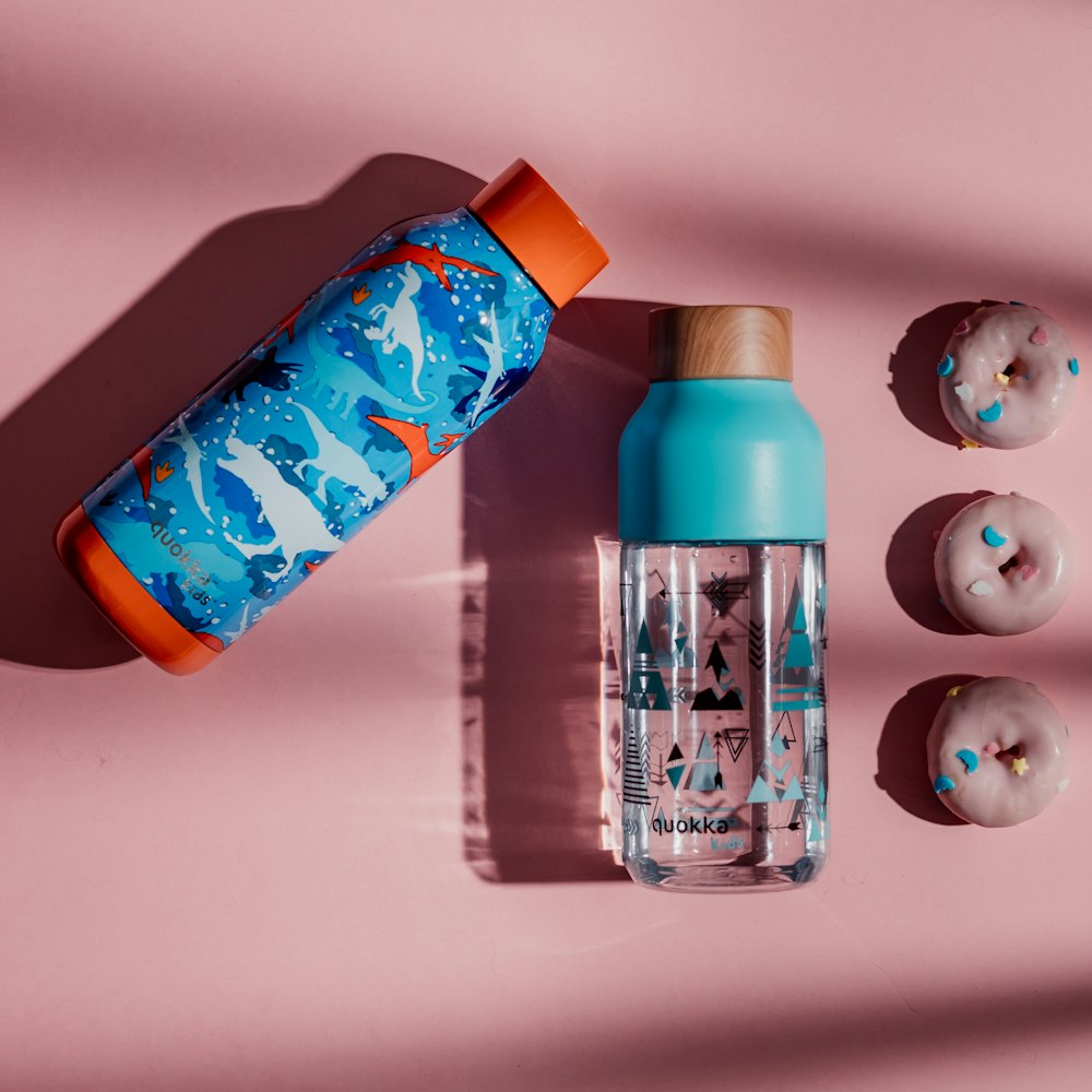 a bottle of water next to three donuts on a pink surface