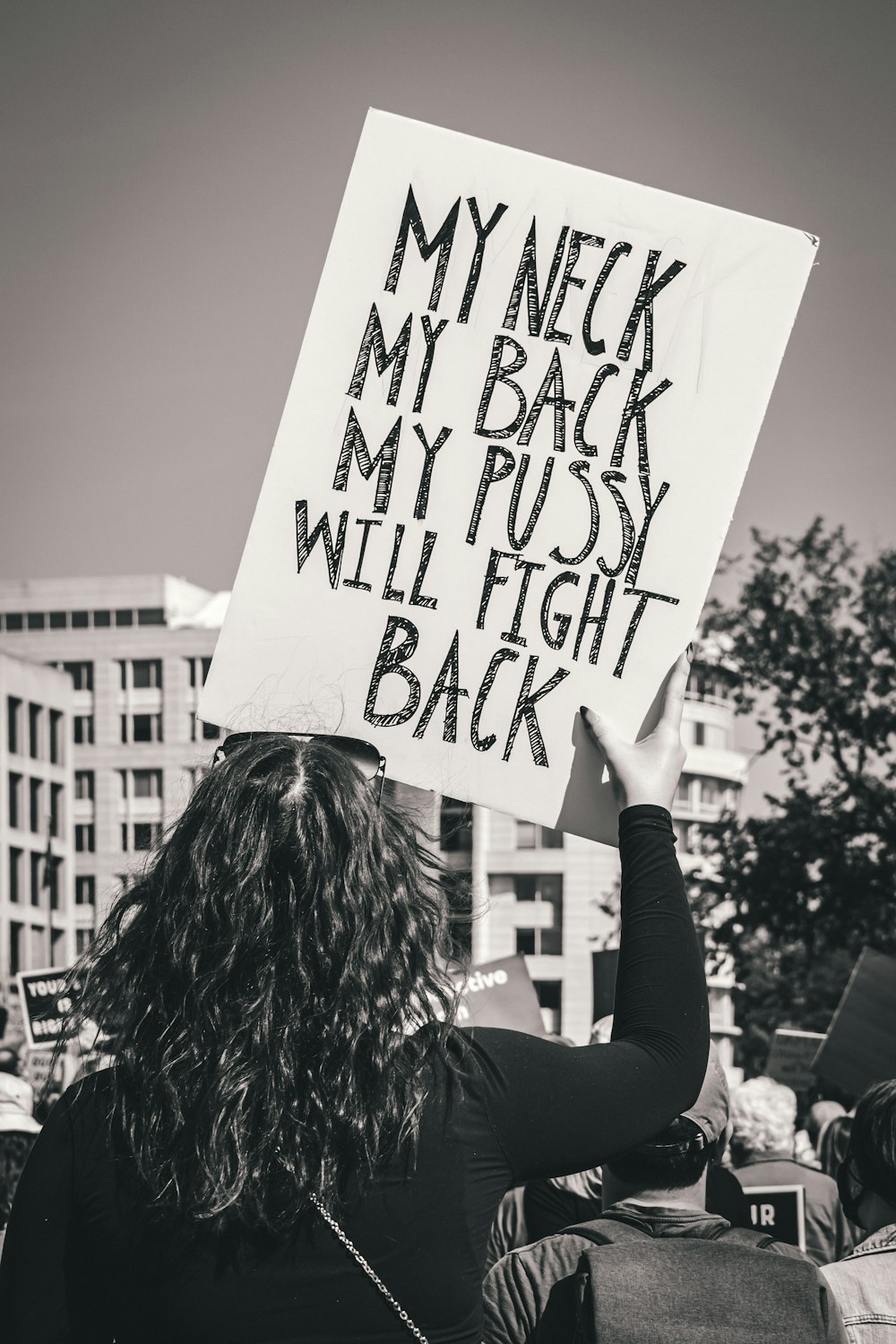 a woman holding a sign that says my neck my back my pussy will fight back