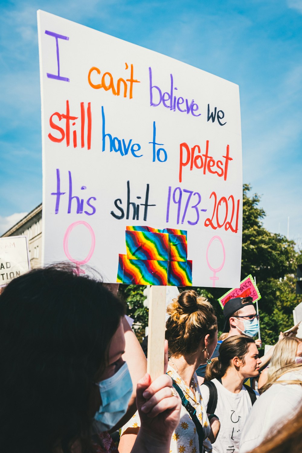 a woman holding a sign that says i can't believe we still have to