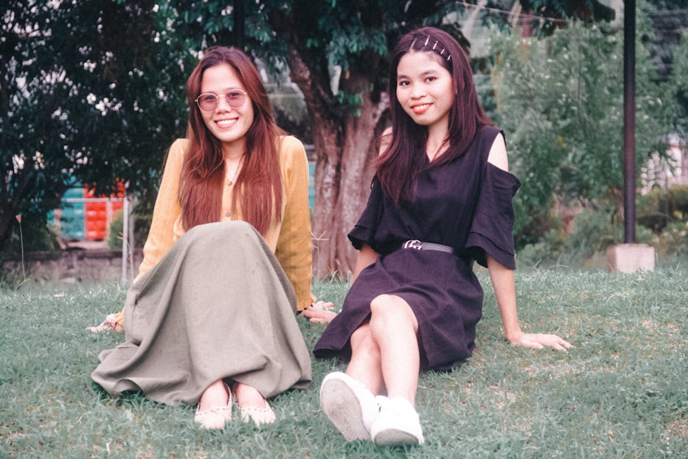 two young women sitting on the grass in a park