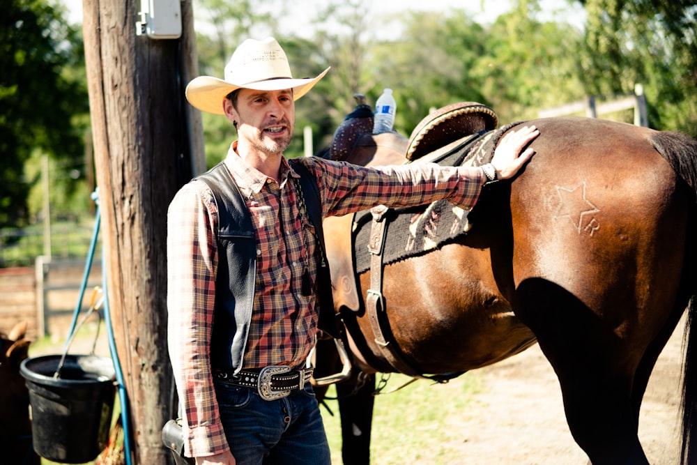 a man in a cowboy hat standing next to a horse