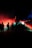 Silhouettes of people standing in a dark space are illuminated by colorful lights. Red and green lights create a dramatic, atmospheric effect with fog or smoke dispersing the beams.