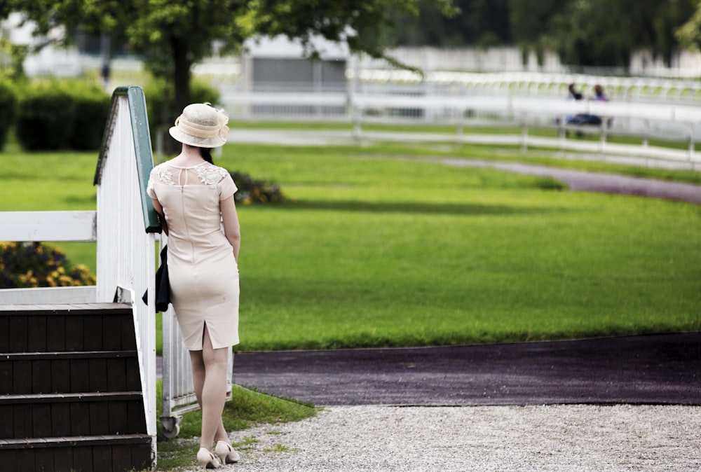 a woman in a dress and hat standing next to a white fence