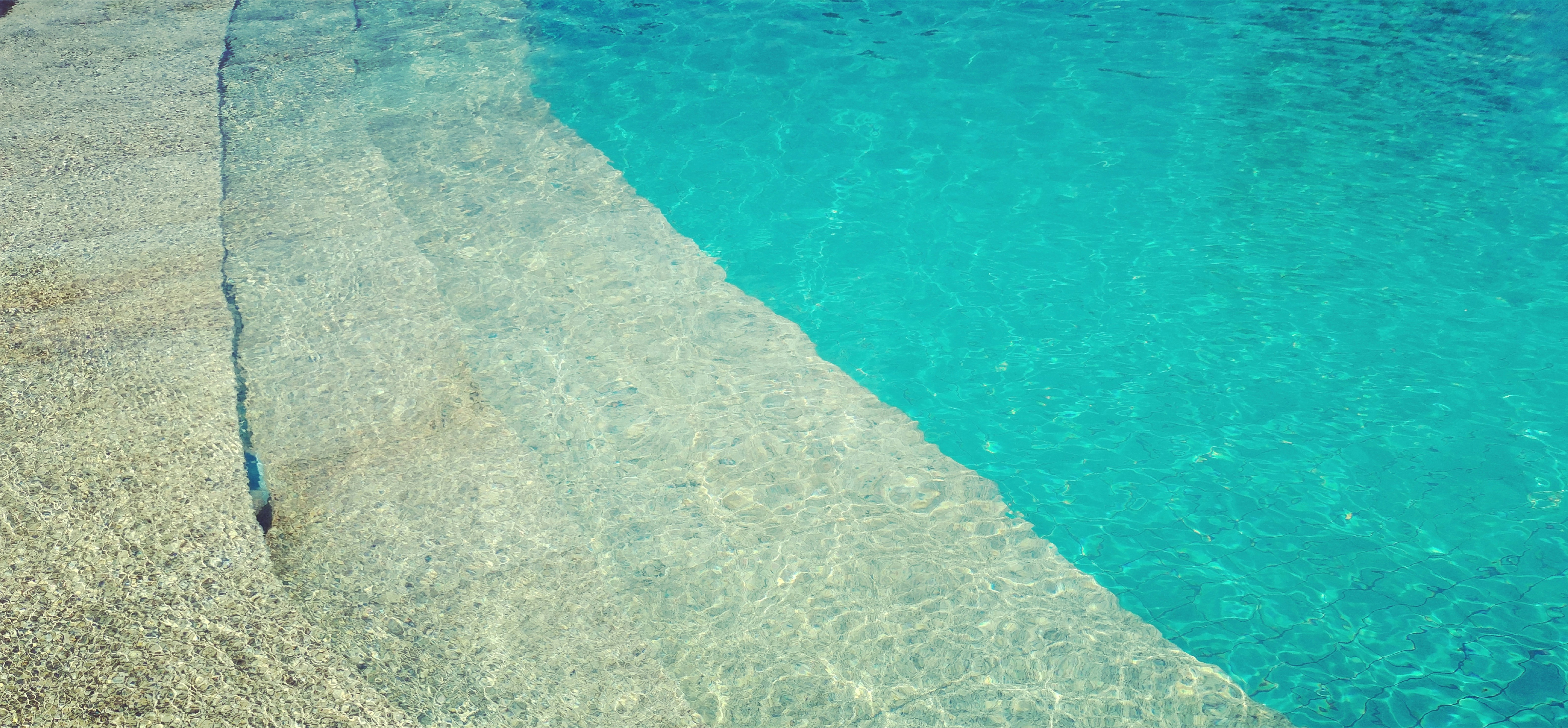 a pool with clear blue water next to a beach