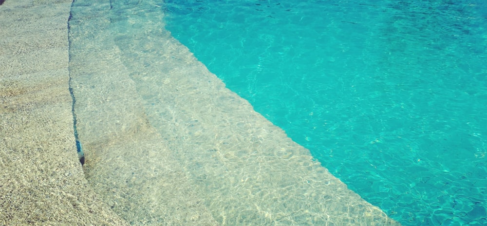 a pool with clear blue water next to a beach