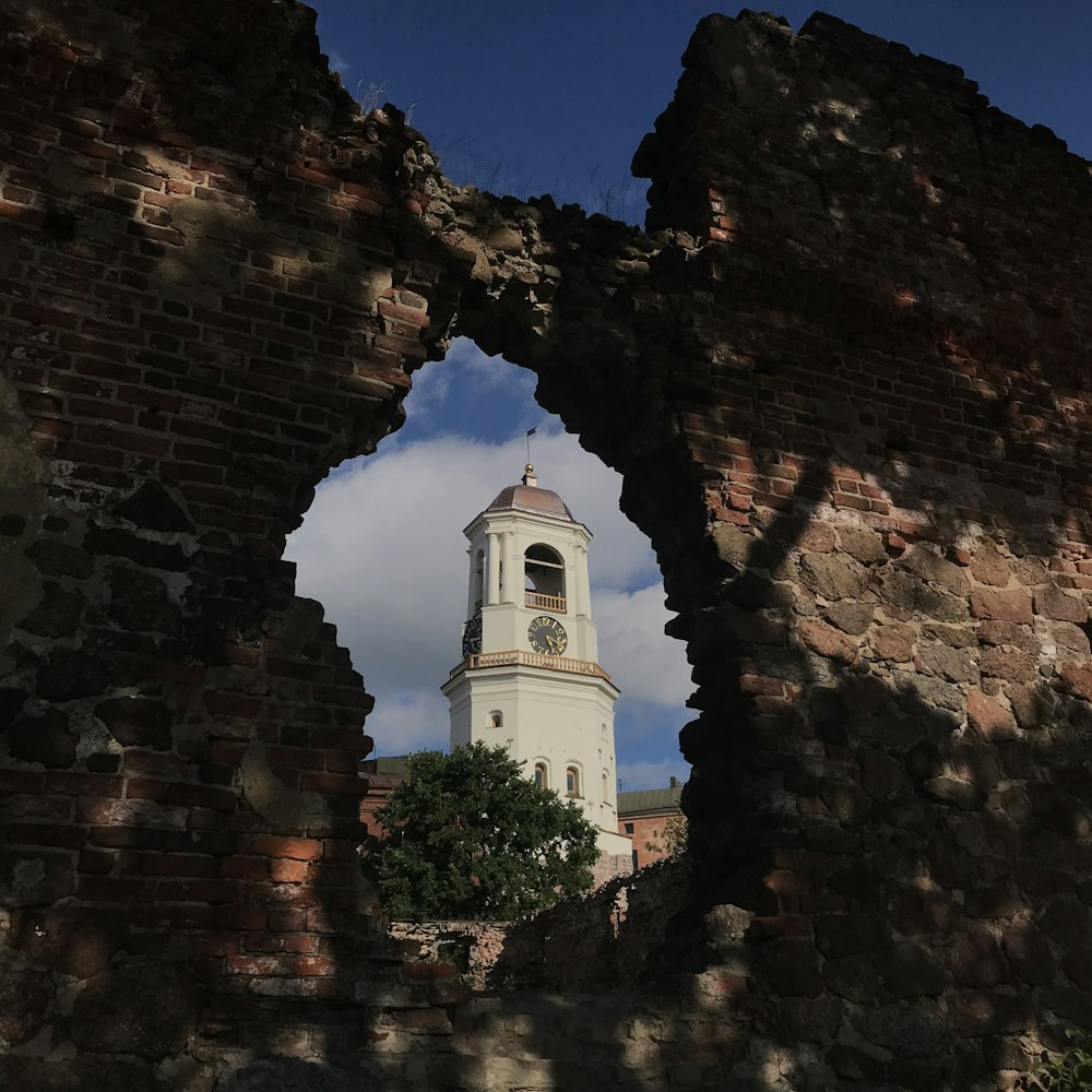 a clock tower seen through a hole in a brick wall