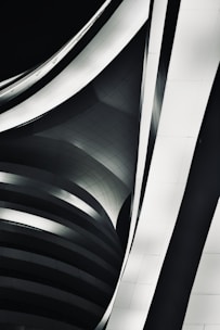 An abstract architectural design featuring overlapping, curved metallic structures with smooth surfaces. The image shows a play of light and shadows creating a sense of depth and movement.