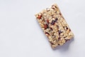 Two granola bars made from oats, nuts, and dried fruits are placed on a light gray background. The texture of the bars appears crunchy with visible almonds and cranberries.