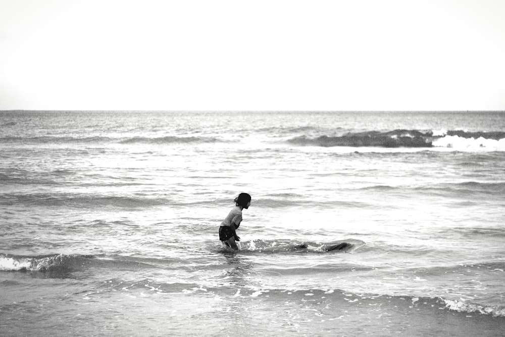 a young boy wading in the ocean on a surfboard