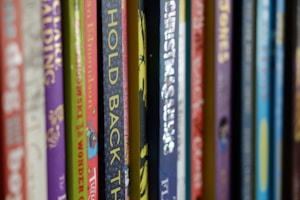 A close-up of hands browsing through a colorful collection of printed books on a shelf.