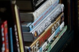 Several books are stacked vertically on a shelf. The titles visible include children's literature, encyclopedias, and travel guides. The spines display a variety of fonts and colorful designs.