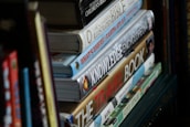 Several books are stacked vertically on a shelf. The titles visible include children's literature, encyclopedias, and travel guides. The spines display a variety of fonts and colorful designs.