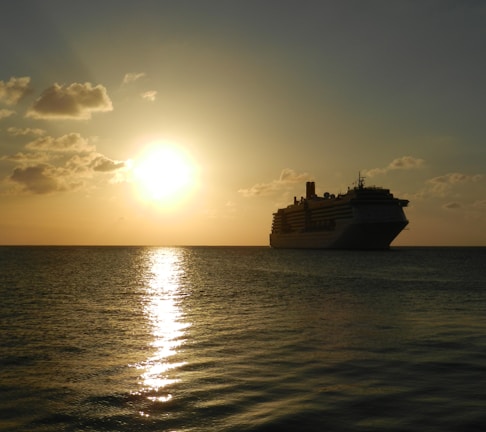 A serene cruise ship sailing past a glowing sunset over calm ocean waters.