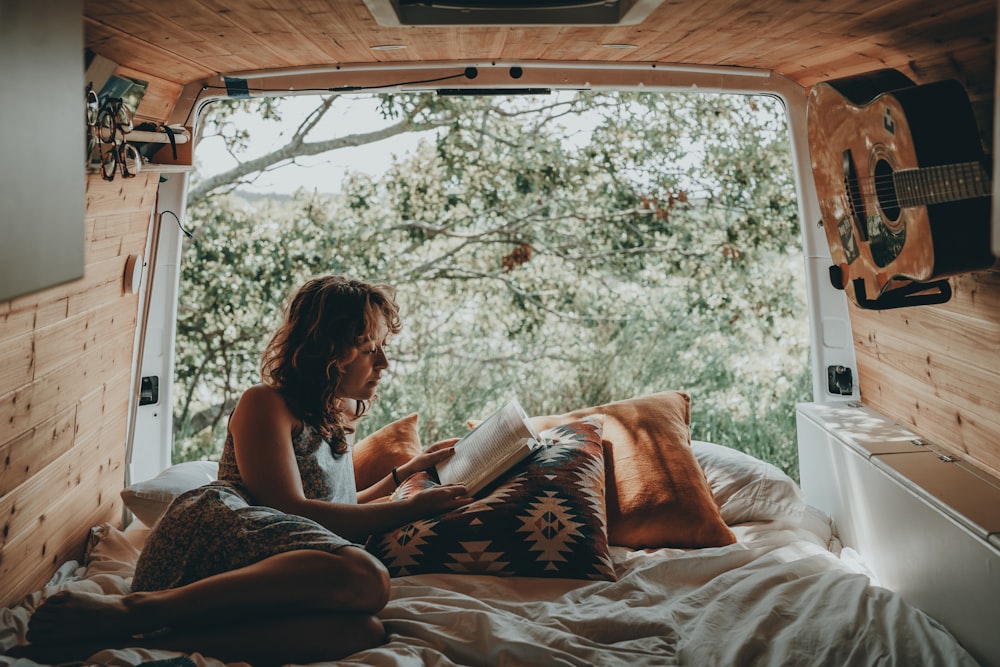 uma mulher sentada em uma cama lendo um livro