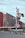 A freight train moves past a railroad crossing with red warning lights activated. The scene includes a metal crossing sign and barrier arm, set against a clear blue sky.