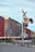 A freight train moves past a railroad crossing with red warning lights activated. The scene includes a metal crossing sign and barrier arm, set against a clear blue sky.