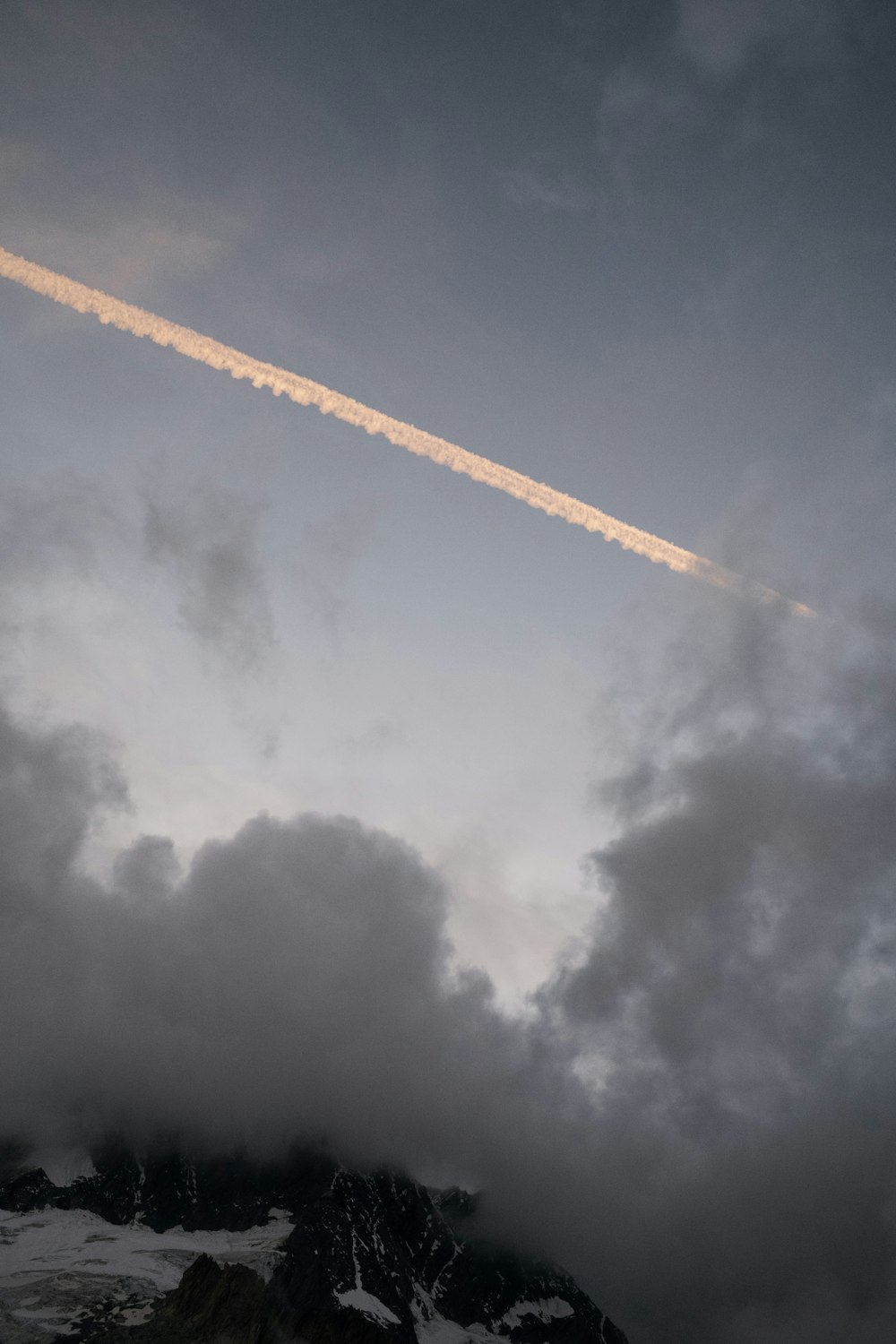 a plane flying through a cloudy sky over a mountain