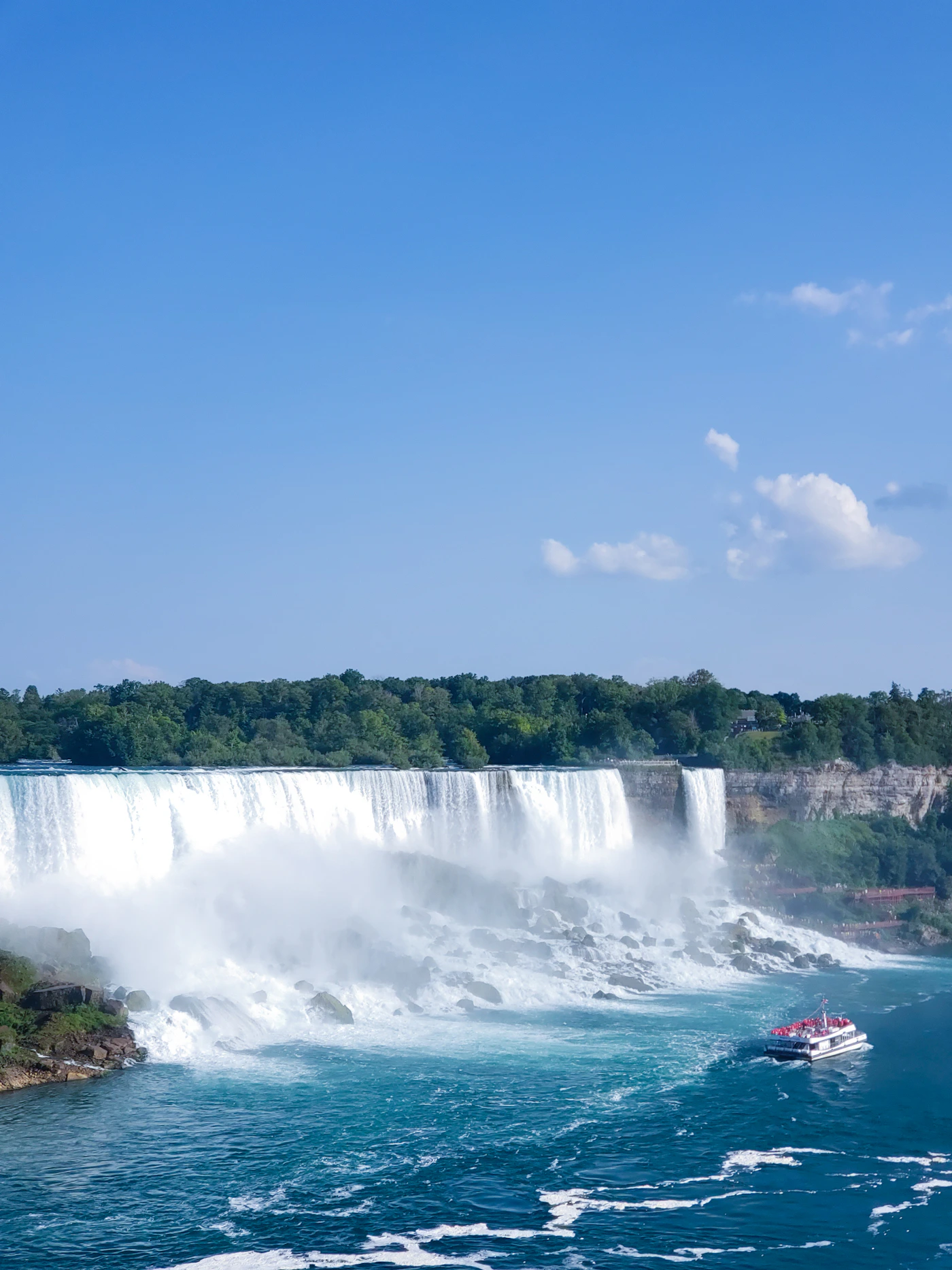 Niagara Falls from the Canadian side, showing the full sweep of the Horseshoe Falls with mist rising and a tour boat approaching the base of the falls