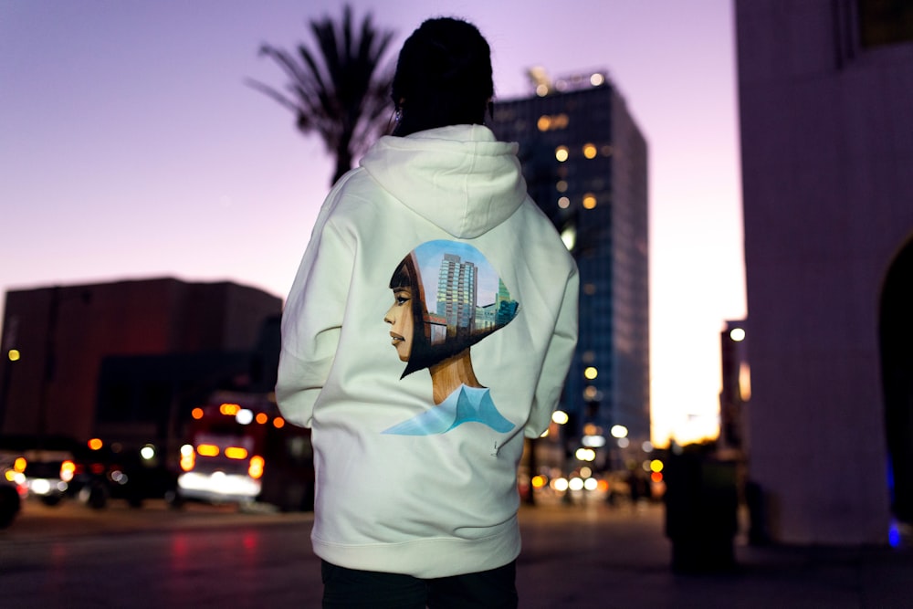 a man in a white hoodie standing in front of a tall building