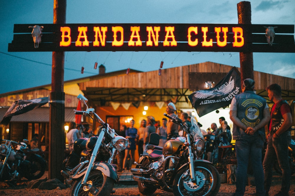 a group of people standing around motorcycles under a sign