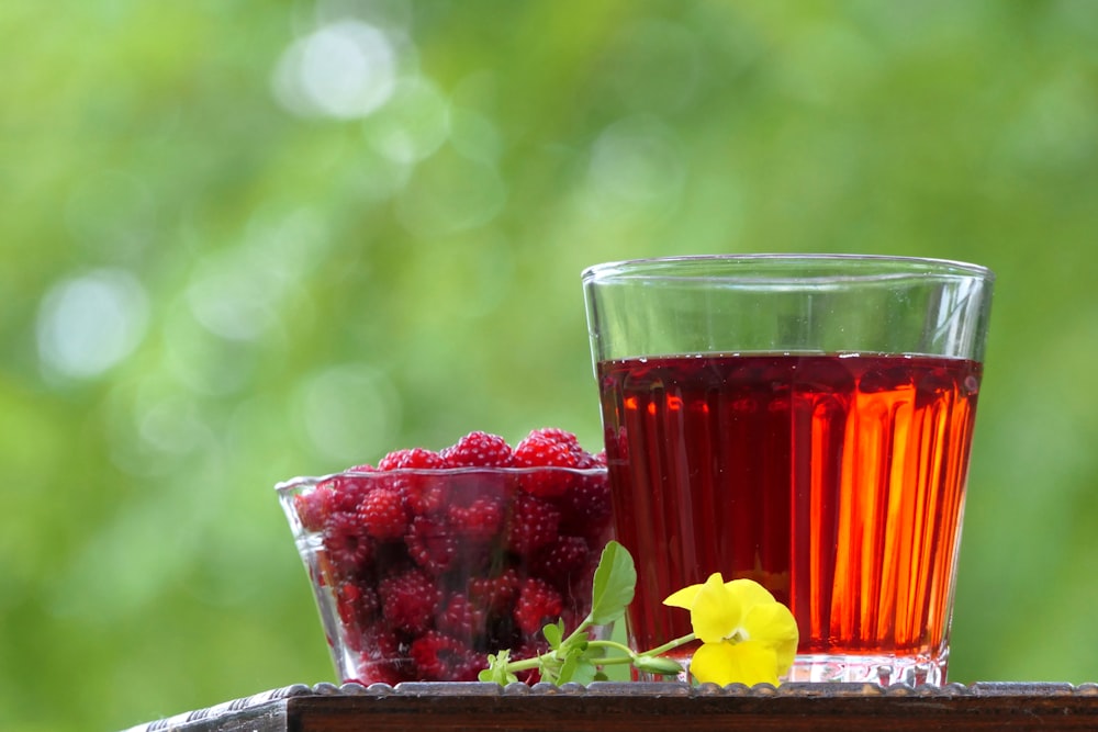 a glass of raspberry tea next to a bowl of raspberries
