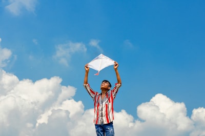 A smiling boy wearing a playful, patterned shirt and shorts set, holding a kite on a breezy day.