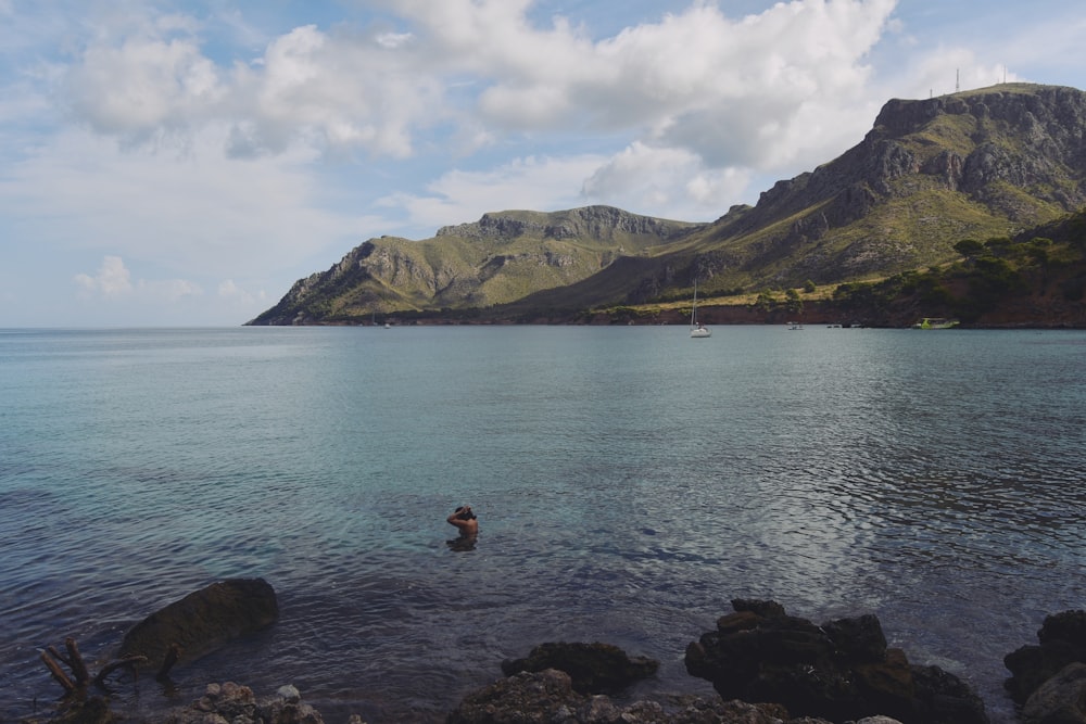 a person wading in the water near a mountain