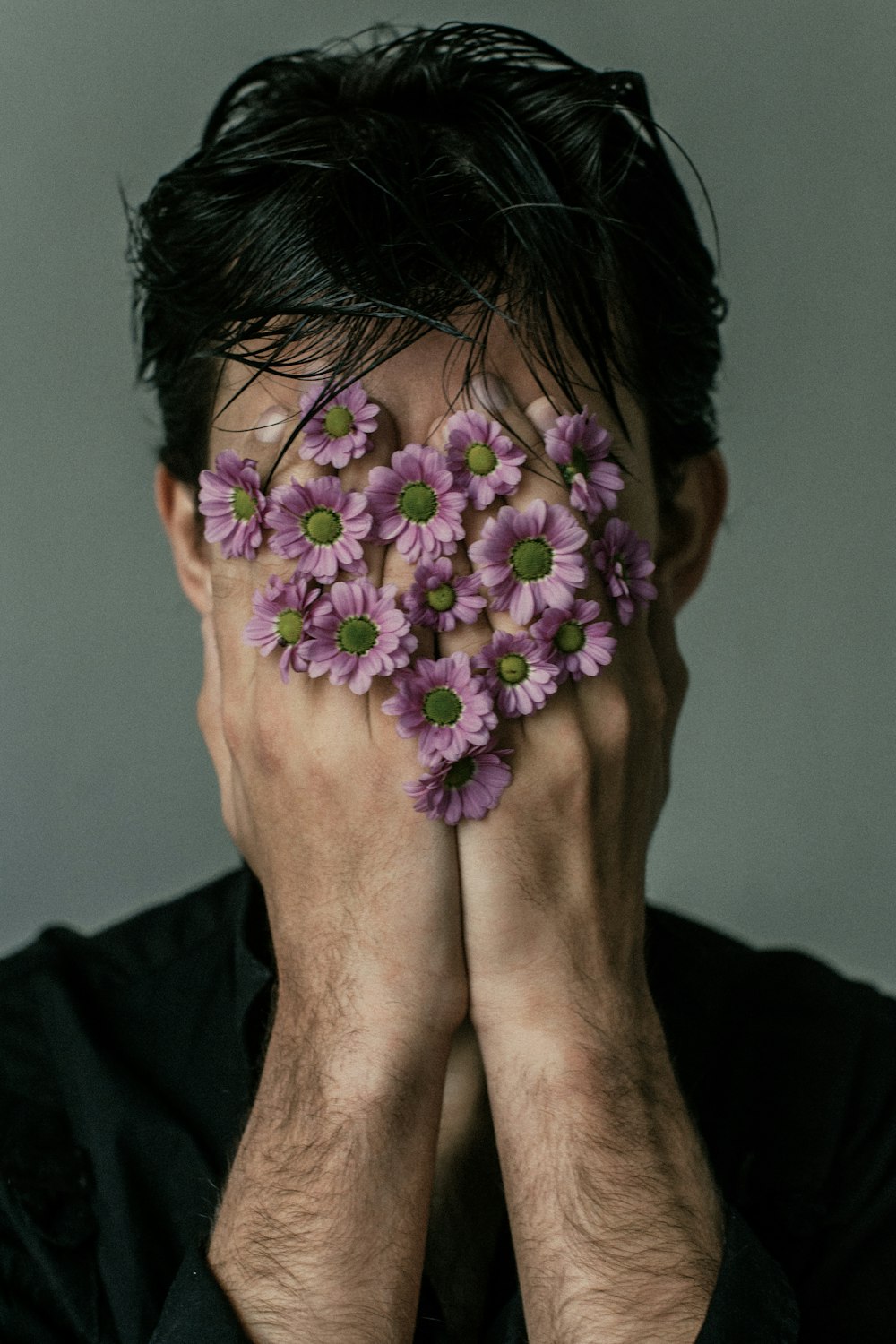 a man covering his face with purple flowers