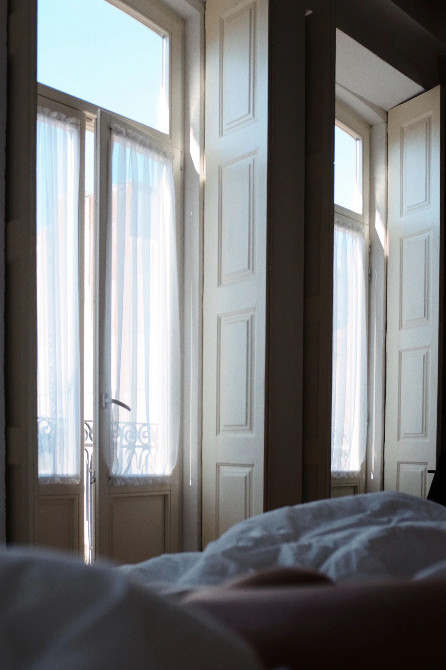 Tall shuttered French windows standing open at the foot of a bed