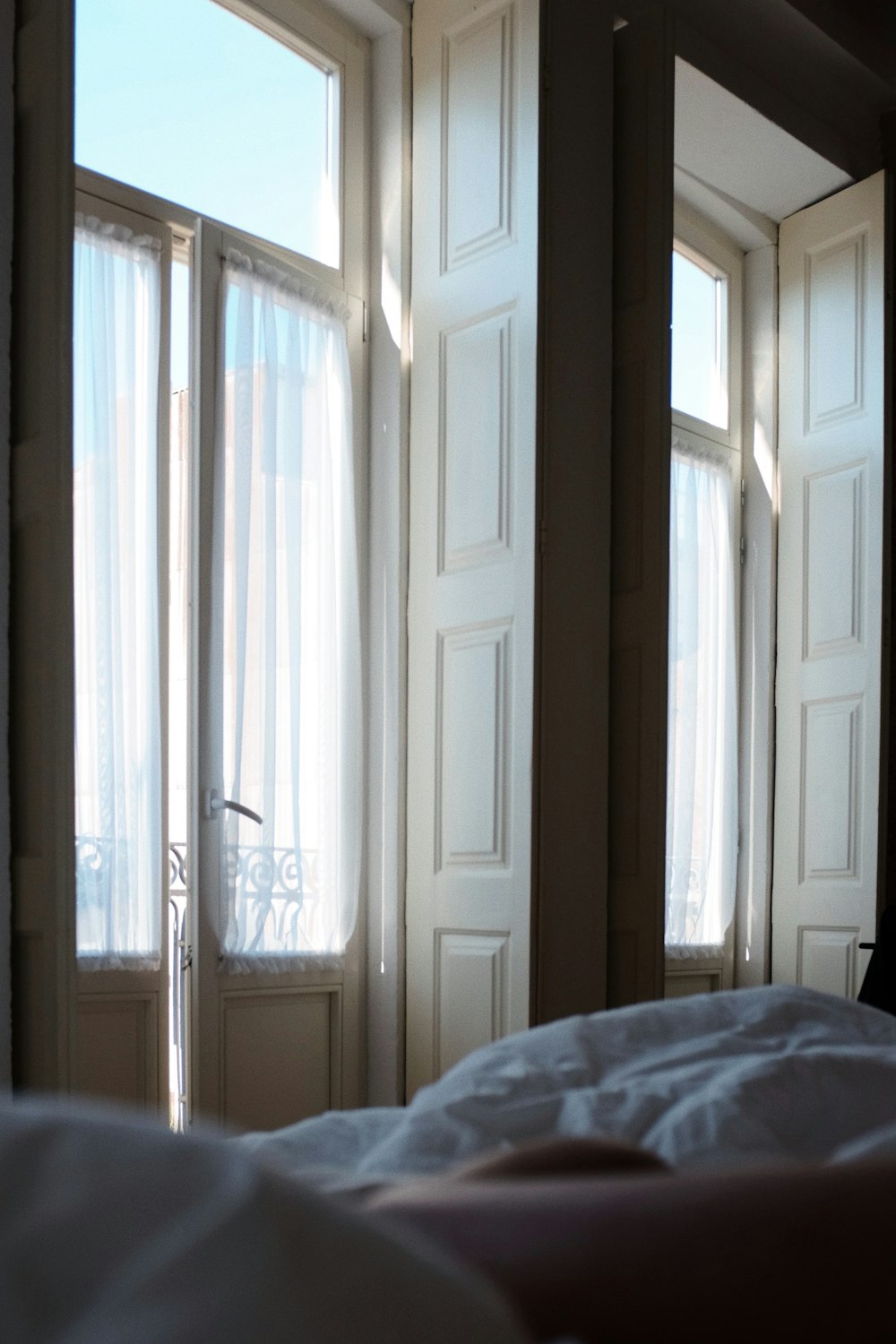 a bed with a white comforter in front of two windows