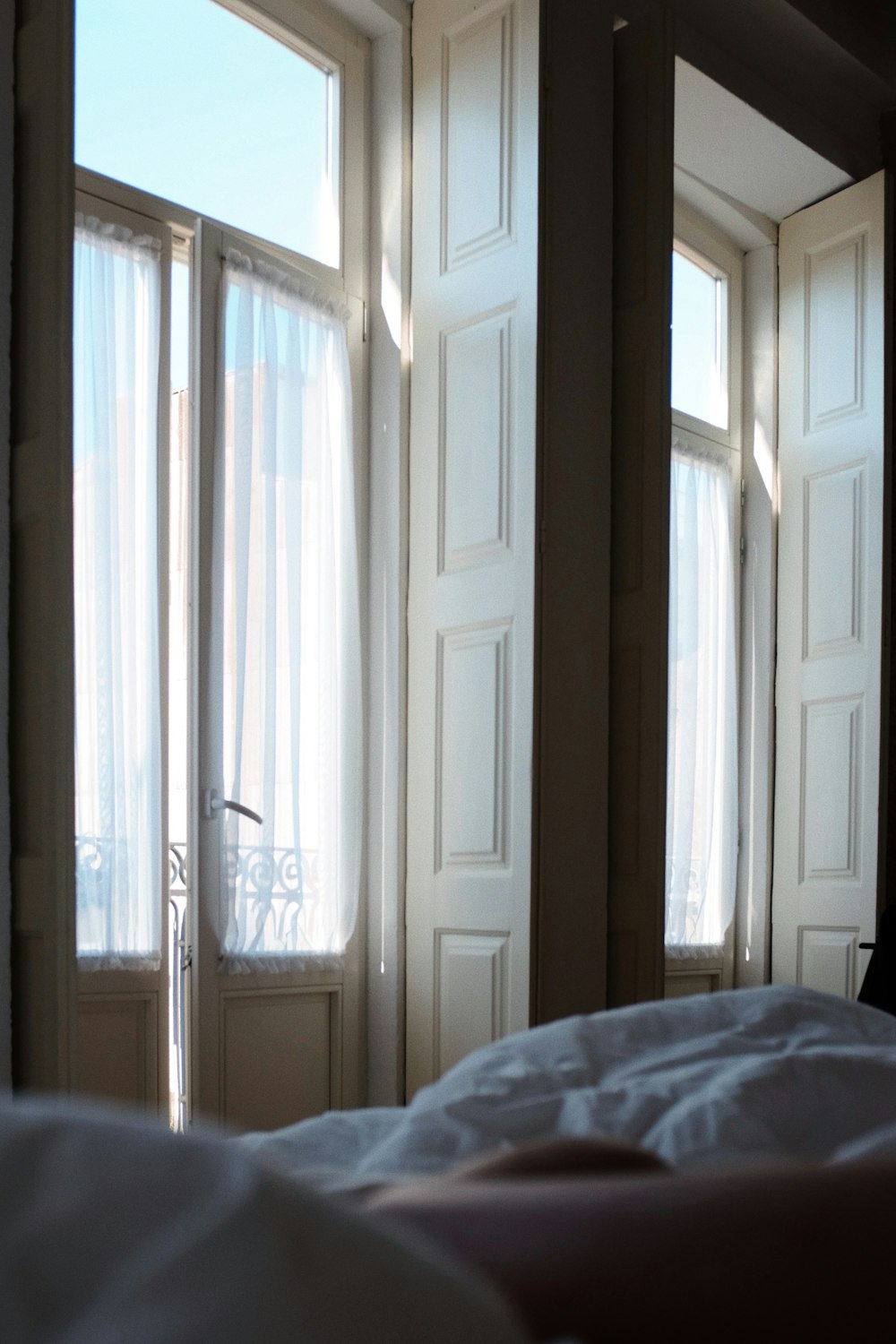 ein Bett mit weißer Bettdecke vor zwei Fenstern