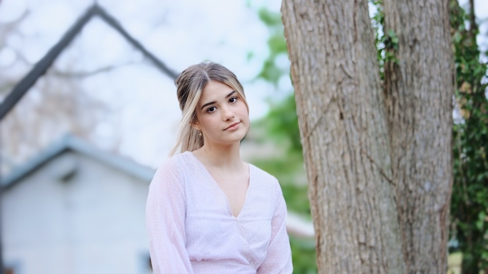 Une femme debout à côté d’un arbre devant une maison