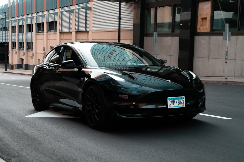 a black car driving down a street next to a tall building