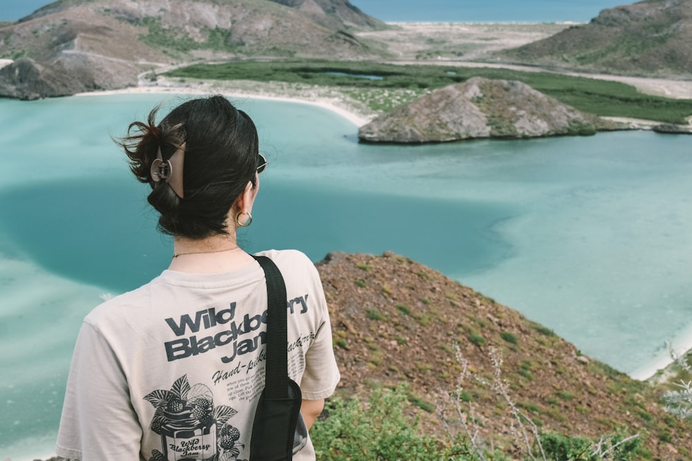 a woman standing on top of a hill looking at a body of water