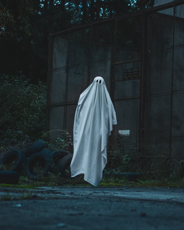 A figure under a white sheet standing in front of a dark building